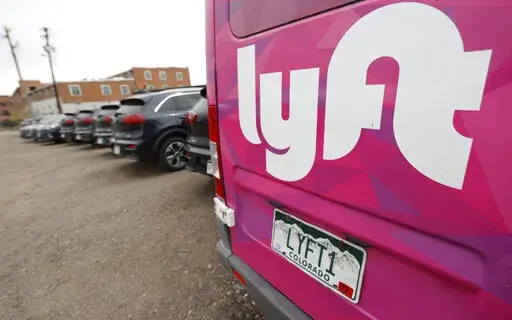 In this April 30, 2020, file photo, Kia Neros that are part of the Lyft ride-hailing fleet sit unused in a lot near Empower Field at Mile High in Denver.  Lyft says it’s adding a fuel surcharge of 55 cents to each ride its drivers perform to help offset recent gasoline price increases. The company said in a blog post on Wednesday, March 16, 2022, that the surcharge will be effective beginning next week, with all of the money going directly from riders to its drivers. (AP Photo/David Zalubowski