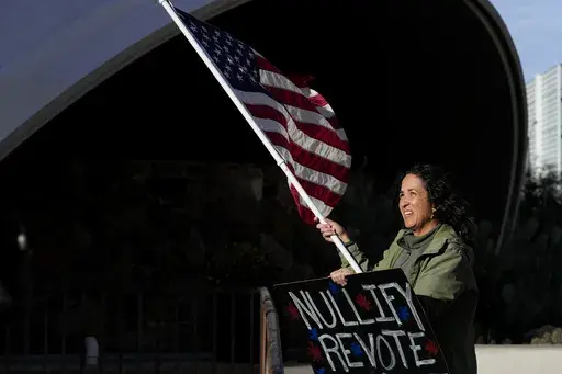 A woman stands in protest outside the Maricopa County Board of Supervisors auditorium prior to the board's general election canvass meeting, Nov. 28, 2022, in Phoenix. A ghost from recent election cycles, controversies over certification of results, is beginning to re-emerge as the nation heads closer to the 2024 presidential contest. (AP Photo/Matt York, File)