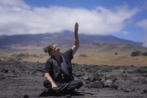 Kealoha Pisciotta, a cultural practitioner and longtime activist, sits on lava rock part of the way up Mauna Kea while giving an interview on the Big Island of Hawaii, on Saturday, July 15, 2023. Over the last 50 years, astronomers have mounted 13 giant astronomical observatories on Mauna Kea's summit. In 2019, Native Hawaiians including Piscioitta staged a year-long protest over construction of an additional telescope. (AP Photo/Jessie Wardarski)