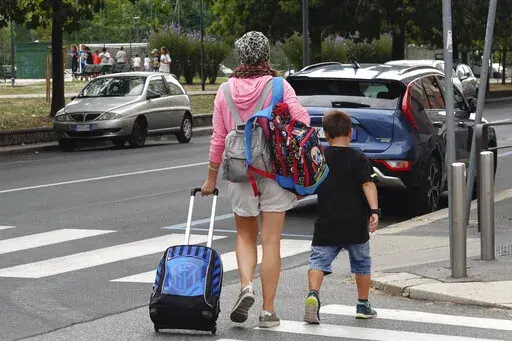 A woman carries backpacks as her son walks after coming out of a primary school, in Milan, Italy, Wednesday, Sept. 14, 2022. Italy could be on the verge of electing its first woman premier. That prospect delights some Italian women, but others are dismayed by her conservative beliefs and policies. If opinion polls prove on the mark, Giorgia Meloni and the far-right Brothers of Italy party she co-founded less than a decade ago will triumph in Sept. 25 elections for Parliament. (AP Photo/Luca Brun