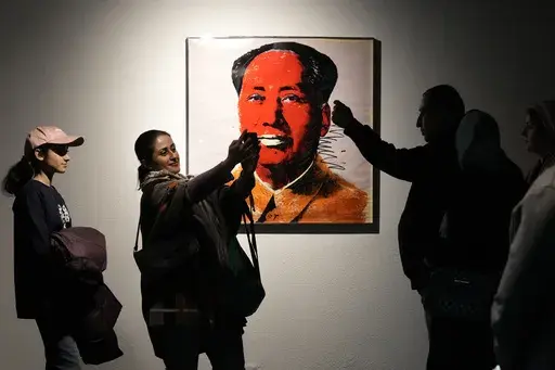 People take snap shots next to China's late leader Mao Zedong painting by American artist Andy Warhol as they visit an exhibition titled Eye to Eye which showcases over 120 works by modern world artists as well as Iranian painters at Tehran Museum of Contemporary Art, in Tehran, Thursday, Nov. 21, 2024. (AP Photo/Vahid Salemi)