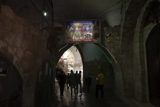 Palestinians walk under a banner depicting militants from the Lions' Den group who were killed by Israeli forces, from left, Fadi Qufesheh, Abdulrahman Soboh, Mohammad Azizi and Mahmoud Zakari, in al-Yasmeena quarter of the Old City of Nablus, in the West Bank, Thursday, May 4, 2023. The killing of Zuhair al-Ghaleeth last month, the first slaying of a suspected Israeli intelligence collaborator in the West Bank in nearly two decades, has laid bare the weakness of the Palestinian Authority and th