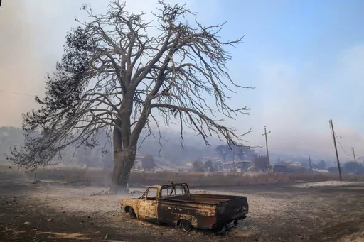 A damaged car stands in front of a burned tree near Loutraki 80 Kilometres west of Athens, Greece, Monday, July 17, 2023. Two wildfires threatened homes in areas outside Athens, where strong winds made the flames difficult to contain. Most of southern Greece, including greater Athens, was an elevated level of alert for fire risk, while more extreme temperatures are expected later this week. (AP Photo/Petros Giannakouris)