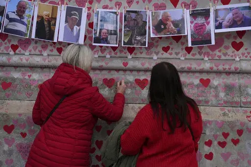 Family members write a message to two sisters who died of COVID on the National Covid Memorial wall in London, Tuesday, March 29, 2022. Latest figures from Britain's statistics agency show the prevalence of COVID-19 in the U.K. has reached record levels, with about 1 in 13 people estimated to be infected with the virus in the past week. Some 4.9 million people were estimated to have the virus in the week ending March 26, up from 4.3 million recorded in the previous week, the Office for National 