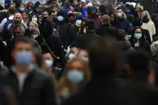 Shoppers walk down Oxford Street, Europe's busiest shopping street, in London, Dec. 23, 2021. The British government confirmed Saturday Feb. 19, 2022, that people with the coronavirus will not be legally required to self-isolate starting next week, as part of a plan for “living with COVID” that is also likely to see testing for the virus scaled back. (AP Photo/Frank Augstein, File)