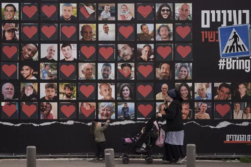 A woman and her children walk past a wall with photographs of hostages who were kidnapped during the Oct. 7 Hamas cross-border attack in Israel in Jerusalem, Israel, Monday, Feb. 26, 2024. (AP Photo/Leo Correa, File)