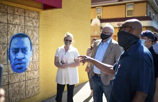Minnesota Gov. Tim Walz, center right, listens to artist Seitu Jones, right, talk about his stencil of George Floyd, in St. Paul, Minn., Monday, June 8, 2020. (Glen Stubbe/Star Tribune via AP, Pool)