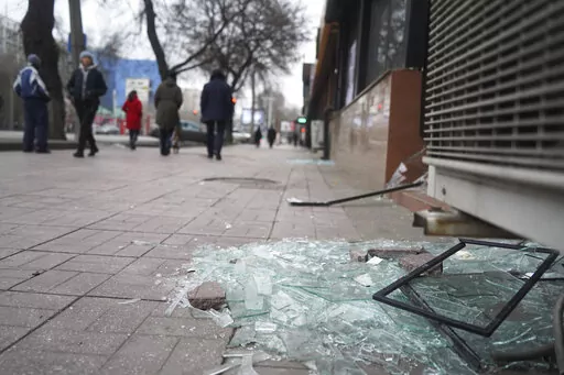 People walk past a shop with windows broken during clashes in Almaty, Kazakhstan, Monday, Jan. 10, 2022. Kazakhstan's health ministry says over 150 people have been killed in protests that have rocked the country over the past week. President Kassym-Jomart Tokayev's office said Sunday that order has stabilized in the country and that authorities have regained control of administrative buildings that were occupied by protesters, some of which were set on fire. (Vladimir Tretyakov/NUR.KZ via AP)