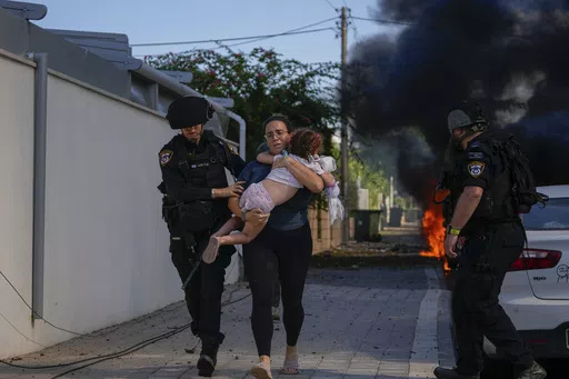 Israeli police officers evacuate a woman and a child from a site hit by a rocket fired from the Gaza Strip, in Ashkelon, southern Israel, Saturday, Oct. 7, 2023. Thousands of Hamas-led militants storm across the border into Israel, killing 1,200 people, mostly civilians, and taking roughly 250 captive, according to Israeli authorities. (AP Photo/Tsafrir Abayov, File)