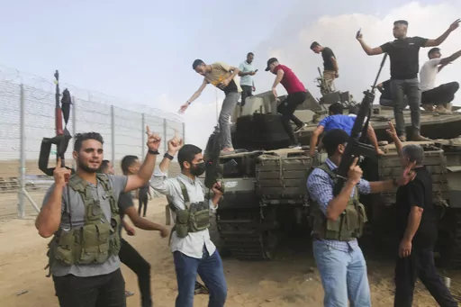 Palestinian militants, some with guns raised in the air, celebrate by an Israeli tank at the border fence of the Gaza Strip on Oct. 7, 2023. The militant Hamas rulers of the Gaza Strip carried out an unprecedented, multi-front attack on Israel at daybreak, firing thousands of rockets as dozens of Hamas fighters infiltrated the heavily fortified border in several locations by air, land, and sea and catching the country off-guard on a major holiday. (AP Photo)