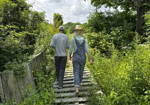 The founders of Fruition Seeds, Matthew Goldfarb, left, and Petra Page-Mann, walk on their farm in Naples, N.Y., on Thursday, Aug. 1, 2024. The multimillion-dollar organic seed company has declared that "seeds are gifts" and will be giving them away after this month. (AP Photo/Cara Anna)