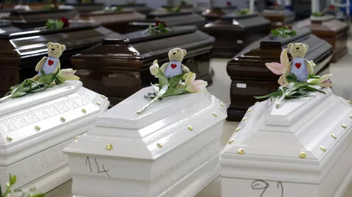 Teddy bears and flowers placed are placed on the coffins of deceased migrants inside a hangar at Lampedusa's airport, Italy, Saturday, Oct. 5, 2013. A decade ago this year, the head of the EU's executive branch, Jose Manuel Barroso stood visibly shaken before hundreds of coffins holding the corpses of migrants drowned off the Italian Island of Lampedusa. (AP Photo/Luca Bruno, File)