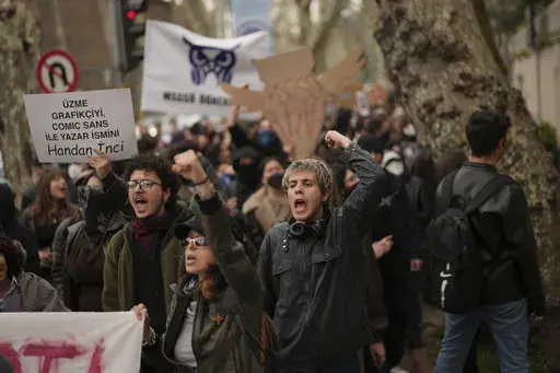 University students shout slogans during a protest after Istanbul's Mayor Ekrem Imamoglu was arrested and sent to prison, in Istanbul, Turkey, Thursday, March 27, 2025. Board on the left reads in Turkish: "Do not upset the graphic artist, he will write your name with Comic Sans, Handan Inci." (AP Photo/Francisco Seco)