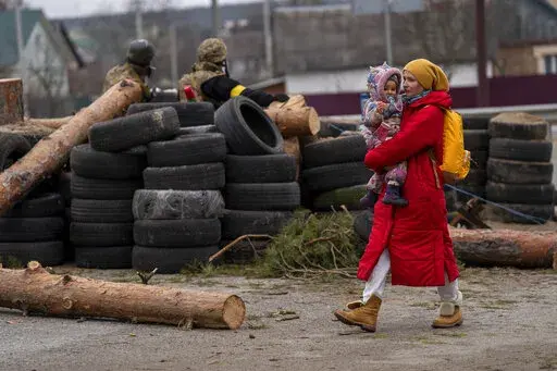 A Ukrainian woman holding a baby walks past a barricade controlled by Ukrainian soldiers as they flee crossing the Irpin river in the outskirts of Kyiv, Ukraine, Saturday, March 5, 2022. (AP Photo/Emilio Morenatti)