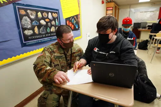 New Mexico Army National Guard specialist Michael Stockwell kneels while helping Alamogordo High School freshman Aiden Cruz with a geology assignment, at Alamogordo High School,Tuesday, Feb. 8, 2022, in Alamogordo, N.M. Dozens of National Guard Army and Air Force troops in New Mexico have been stepping in for an emergency unlike others they have responded to before: the shortage of teachers and school staff members that have tested the ability of schools nationwide to continue operating during t