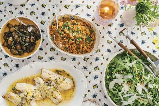 This image released by Celadon Books shows a table spread featuring a red rice dish, top center, from the cookbook "Does This Taste Funny: Recipes Our Family Loves" by Stephen Colbert and Evie McGee Colbert. (Eric Wolfinger/Celadon Books via AP)