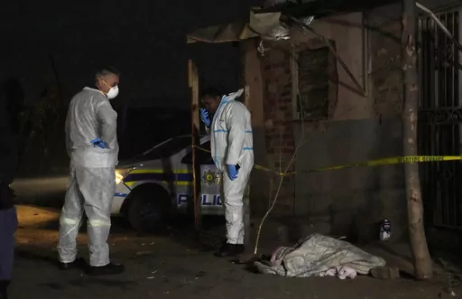 Police stand near a covered body in the Angelo settlement in Boksburg, South Africa, Thursday, July 6, 2023. Police said over a dozen people, including children, have died from a toxic gas leak in the informal settlement. (AP Photo/Themba Hadebe)