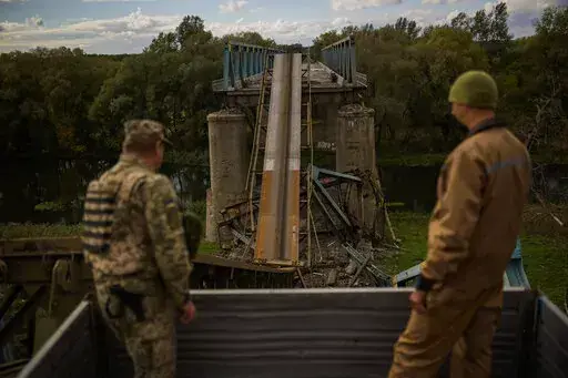 Ukrainian soldiers remove metal structure pieces as they work on a bridge damaged during fighting with Russian troops in Izium, Ukraine, Monday, Oct. 3, 2022. A series of embarrassing military losses for Moscow in recent weeks has presented a growing challenge for prominent hosts of Russian news and political talk shows scrambling to find ways to paint Kyiv's gains in a way that is still favorable to the Kremlin. (AP Photo/Francisco Seco)