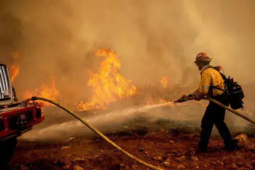 A firefighter sprays water while trying to keep the Electra Fire from spreading in the Pine Acres community of Amador County, Calif., on Tuesday, July 5, 2022. (AP Photo/Noah Berger)
