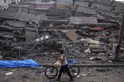A Palestinian child walks with a bicycle by the rubble of a building after it was hit by an Israeli airstrike, in Gaza City, Sunday, Oct. 8, 2023. A new U.N. report paints a stark picture of the devastating collapsing Palestinian economy after a month of war and Israel’s near total siege of Gaza. (AP Photo/Fatima Shbair, File)