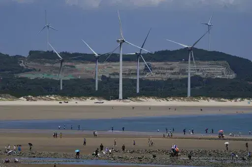 Beachgoers walk near wind turbines along the coast of Pingtan in Southern China's Fujian province, on Aug. 6, 2022. The world's two biggest emitters of greenhouse gases are sparring on Twitter over climate policy, with China asking if the U.S. can deliver on the landmark climate legislation signed into law by President Joe Biden this week. (AP Photo/Ng Han Guan)