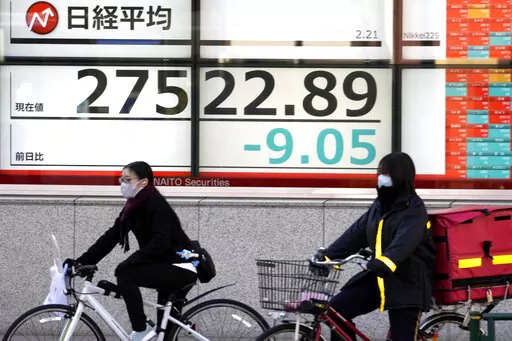 People on bicycle wait to cross a street in front of an electronic stock board showing Japan's Nikkei 225 index at a securities firm Tuesday, Feb. 21, 2023, in Tokyo. Asian shares were mostly lower Tuesday in quiet trading after U.S. markets were closed for Presidents Day. (AP Photo/Shuji Kajiyama)