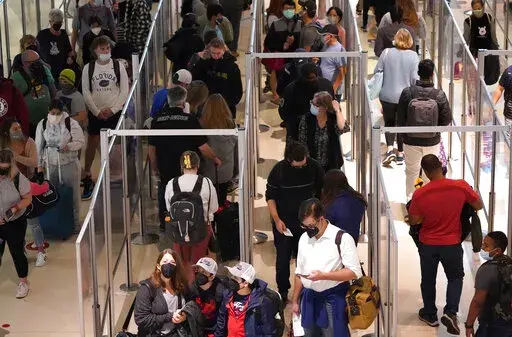 To prevent the spread of COVID-19, air travelers wear masks and are separated by plexiglass as they make their way through security at Love Field in Dallas, Friday, Dec. 31, 2021. Flight cancellations surged again on the last day of 2021, with airlines blaming it on crew shortages related to the spike in COVID-19 infections.  (AP Photo/LM Otero)