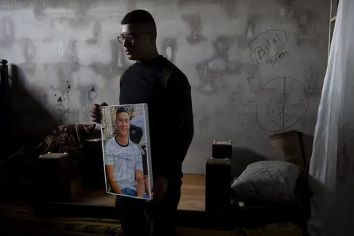 Yousef Mesheh, 15, holds a portrait of his brother, Wael in the bedroom where they were sleeping when Israeli forces stormed into their home at 3.a.m., in the Balata Refugee Camp in the northern West Bank, Tuesday, Jan. 10, 2023. They were both arrested, but Wael is still imprisoned. A report to be released next Monday by Israeli human rights organization HaMoked found that the Israeli military arrested and interrogated hundreds of Palestinian teenagers in 2022 in the occupied West Bank, without