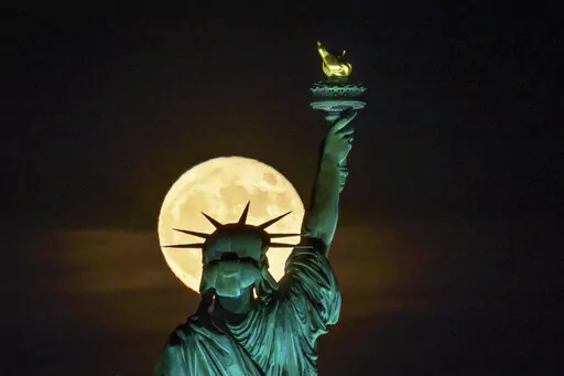 The Strawberry Supermoon rises in front of the Statue of Liberty in New York, late Tuesday, June 14, 2022. (AP Photo/J. David Ake)
