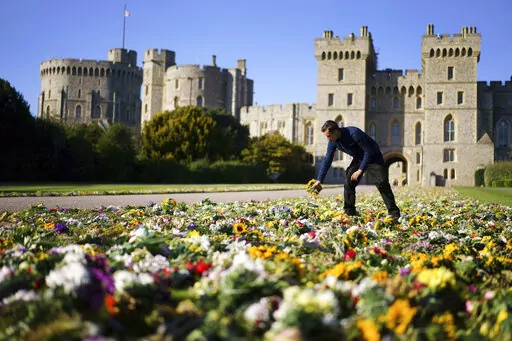 Workers from the Crown Estate move the floral tributes laid by members of the public outside Windsor Castle onto Cambridge Drive, near the Long Walk, Windsor, Sunday Sept. 18, 2022 ahead of the funeral of Queen Elizabeth II on Monday. (Victoria Jones/PA via AP)