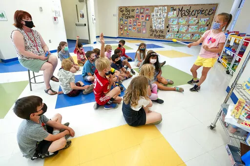 FILE — Kelly Sheridan, left, and her first grade students wear face masks as one of the students makes a presentation during class in a hallway at the Milton Elementary School, May 18, 2021, in Rye, N.Y. The New York State Education Department is telling schools to continue to require masks despite a judge’s ruling overturning the state's mask mandate.  But some school districts already are rushing to drop the requirement.  The Education Department said in a statement Tuesday, Jan. 25, 202