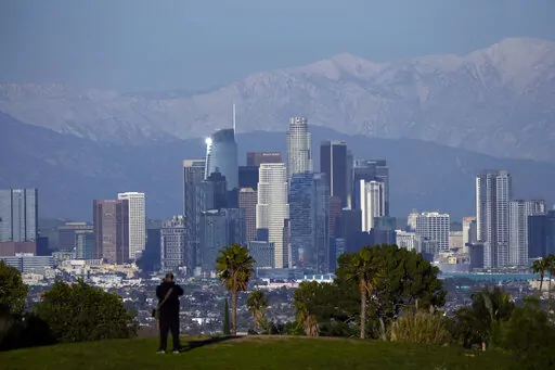 A visitor takes in a view of the city's skyline under the snow-covered San Gabriel mountains after a series of storms Thursday, March 2, 2023, in Los Angeles. (AP Photo/Marcio Jose Sanchez)