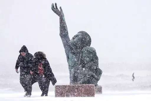 People walk past the 1900 Storm memorial sculpture on Seawall Blvd. during an icy winter storm on Tuesday, Jan. 21, 2025 in Galveston, Texas. (Brett Coomer/Houston Chronicle via AP)
