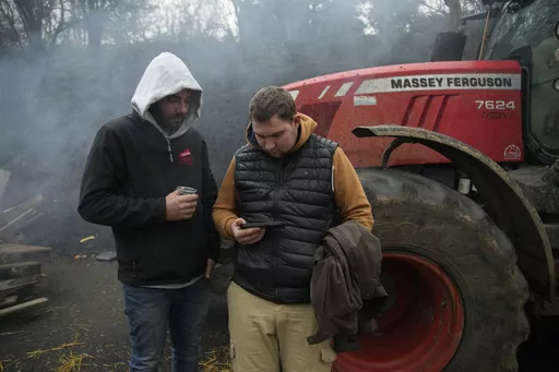 Farmers watch French Prime Minister Gabriel Attal on a smartphone, announcing new measures for farmers, on a blocked highway, Thursday, Feb.1, 2024 in Chilly-Mazarin, south of Paris. Protests have been held across the EU for most of the week and hundreds of angry farmers driving heavy-duty tractors arrived at European Union headquarters, bent on getting their complaints about excessive costs, rules and bureaucracy heard and fixed by EU leaders at a summit Thursday in Brussels, Belgium. (AP Photo