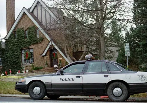 A police officer sits in her cruiser, Jan. 3, 1997, outside the home in which 6-year-old JonBenet Ramsey was found murdered in Boulder, Colo., on Dec. 26, 1996. (AP Photo/David Zalubowski, File)