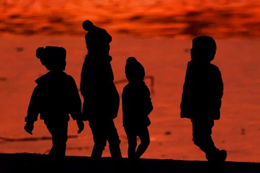 Kids are silhouetted against a pond at a park in Lenexa, Kan., on Saturday, Dec. 26, 2020. Health officials remain perplexed by mysterious cases of severe liver damage in hundreds of young children around the world. In May 2022, the U.S. Centers for Disease Control and Prevention officials said they are now looking into 180 possible cases across the U.S. More than 20 other countries have reported hundreds more cases in total, though the largest numbers have been in the U.K. and U.S. (AP Photo/Ch
