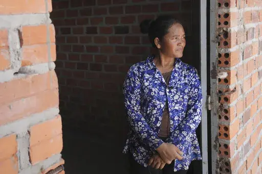 Chhem Hay, 37, stands at a main door of her house under construction at Run Ta Ek village in Siem Reap province, Cambodia, on April 2, 2024. She decided last June to take the opportunity to move from the village where she'd lived since she was a young teenager to the new settlement. Cambodia's program to relocate people living on the famous Angkor archaeological site is drawing international concern over possible human rights abuses, while authorities maintain they're doing nothing more than pro