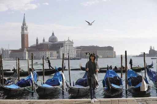 A tourist takes a selfie in St. Mark's Square in Venice, Italy, Nov. 12, 2016. Starting in January, Venice will oblige day-trippers to make reservations and pay a fee to visit the historic lagoon city. On many days, the heart of Venice is overwhelmed by visitors, who often far outnumber residents. Venice officials on Friday unveiled new rules for day-trippers, which go into effect on Jan. 16, 2023. (AP Photo/Luca Bruno, File)