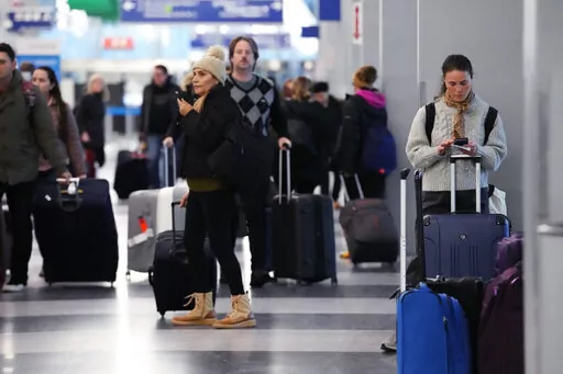A traveler, right, checks on her cellphone as other travelers walk through Terminal 3 at O'Hare International Airport in Chicago, Thursday, Dec. 22, 2022. (AP Photo/Nam Y. Huh)