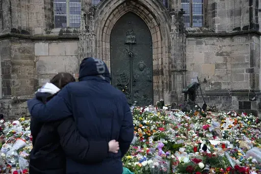 A couple embrace each other in front of flowers and candles laid down at the Johannis church close to the Christmas market, where a car drove into a crowd on Friday evening, in Magdeburg, Germany, Sunday, Dec. 22, 2024. (AP Photo/Ebrahim Noroozi)