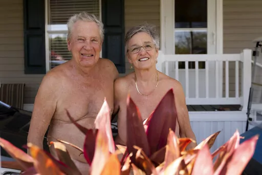 In this image provided by the Religion News Service , Bill and Misty Katz pose in front of their home at Nature's Resort on March 16, 2022, in Elsa, Texas. Bright orange letters welcome you to “Nature’s Resort.” Nothing looks amiss, except for what’s missing — clothing.  (Jeremy Lindenfeld/Religion News Service via AP)