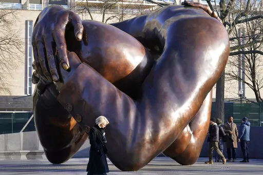 Passers-by walk near the 20-foot-high bronze sculpture "The Embrace," a memorial to Dr. Martin Luther King Jr. and Coretta Scott King, in the Boston Common, Tuesday, Jan. 10, 2023, in Boston. The sculpture, consisting of four intertwined arms, was inspired by a photo of the Kings embracing when MLK learned he had won the Nobel Peace Prize in 1964. The statue is to be unveiled during ceremonies Friday, Jan. 13, 2023. (AP Photo/Steven Senne)