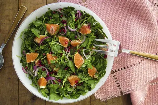 This 2017 image shows a salad recipe with arugula orange slices and pomegranate seeds. (Katie Workman via AP)