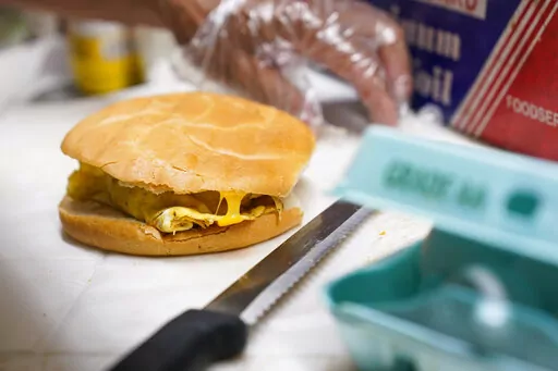 Hector Perez prepares to wrap a bacon, egg and cheese sandwich at a bodega in the Bronx section of New York, Friday, July 22, 2022. While some travelers cringe at the thought of greasy sausages and bland eggs served at the free hotel breakfast buffet, others say free breakfast ranks among their favorite aspects of travel. Hilton says “free breakfast” is the most used search filter on its website. In 2023, some hotels are revamping their offerings to try to change the minds of even the most s
