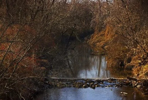 Water flows in Coldwater Creek on Thursday, Dec. 9, 2021, behind a row of homes at Belcroft Drive and Old Halls Ferry Road in Missouri's St. Louis County. Environmental investigation consultants have found significant radioactive contamination at an elementary school, which sits in the flood plain of Coldwater Creek which was contaminated by nuclear waste from weapons production during World War II. (Christian Gooden/St. Louis Post-Dispatch via AP)