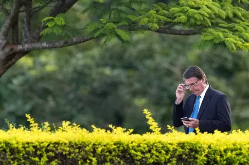 Brazil's President Jair Bolsonaro looks at his cell phone as he arrives for a flag raising ceremony outside Alvorada palace, in Brasilia, Brazil, Thursday, March 17, 2022. (AP Photo/Eraldo Peres)