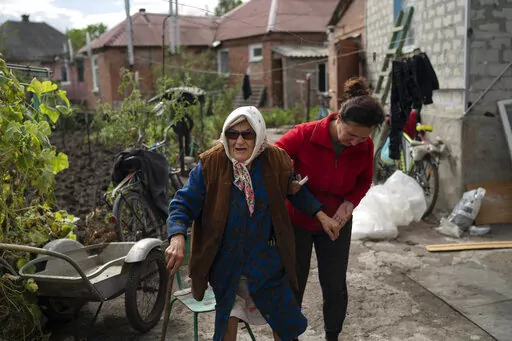 Mariia Ruban, 92, is helped by a neighbor as she stand at garden of her house that damaged its roof and windows after a Russian attack in Sloviansk, Ukraine, Tuesday, Sept. 6, 2022. "I have lived through everything, even starvation. But I have never seen anything like this, like what happened today," says Ruban, supporting herself on a rough wooden cane as she stood in her garden. (AP Photo/Leo Correa)