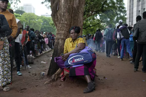 A woman takes a break from the queue outside the passport offices in Harare, Wednesday, Dec. 20, 2023. Atop many Christmas wish lists in economically troubled Zimbabwe is a travel document and people are flooding the passport office this holiday season ahead of a price hike planned in the New Year. The desperation at the office in the capital is palpable as some people fear the hike could push the cost of obtaining a passport out of reach and economic gloom feeds a surge in migration. (AP Photo/