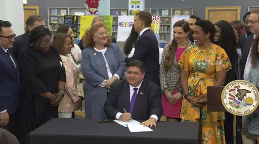 In this screenshot from a livestream broadcast by the State of Illinois, Gov. J.B. Pritzker signs a bill, Monday, June 12, 2023, at Harold Washington Library's Thomas Hughes Children's Library in downtown Chicago. The new law will require the state's libraries to uphold a pledge not to ban material because of partisan disapproval, starting on Jan. 1, 2024. If they refuse, they will not receive state funding. Pritzker said the law will make Illinois the first state in the nation to outlaw book ba