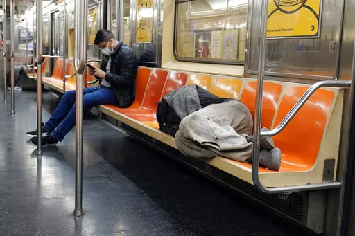 A man sleeps on subway train seats, in New York, on April 14, 2021.New York Mayor Eric Adams is announcing a plan to boost safety in the city's sprawling subway network and try to stop homeless people from sleeping on trains or living in stations. (AP Photo/Richard Drew, File)